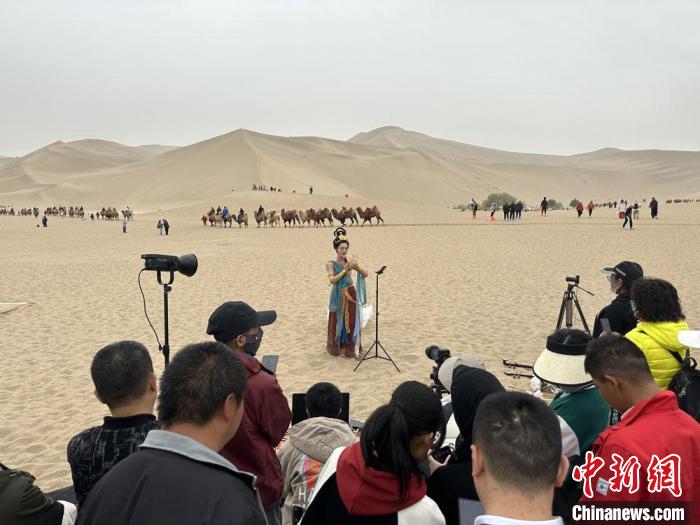 圖為2023年4月底，敦煌大漠“逐舞者”奧楠在鳴沙山月牙泉景區(qū)視頻直播，吸引游人圍觀?！●T志軍 攝